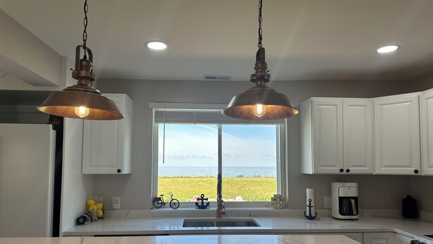 Una cocina con una isla grande, armarios blancos y vista al océano.