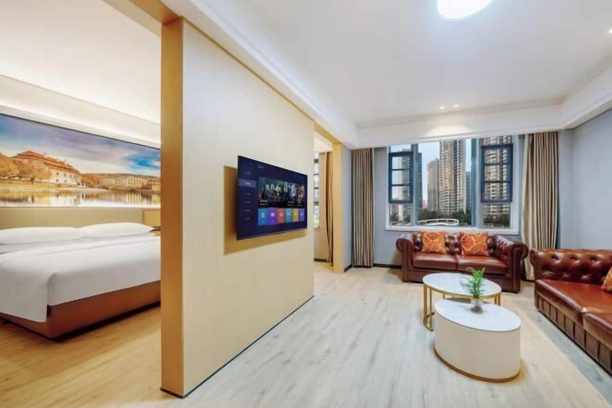 Habitación de hotel con cama, televisión, sofá, mesa de centro y ventana con vista a la ciudad.