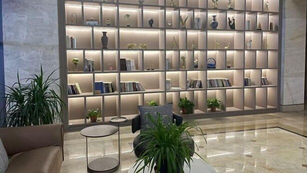 Recepció moderna amb una paret gran i il·luminada plena de llibres i objectes decoratius. Hi ha una zona de seients amb un sofà i una taula rodona petita.