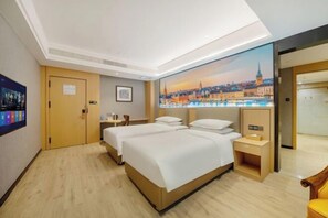 A hotel room with two beds, a painting of a cityscape, a wooden floor, and a small table with a lamp. - Vienna Classic Hotel (Hefei Shushan) (Hefei)
