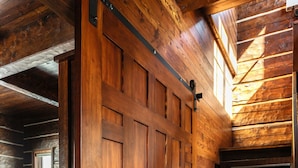 A wooden staircase with a metal handrail leading to a bedroom with a bed, a nightstand, and a window.