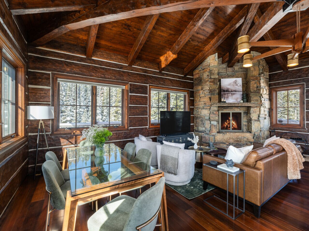 Een gezellig interieur van een chalet met een stenen open haard, houten balken en een eethoek met een glazen tafel.