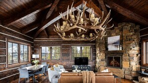 Een rustiek houten interieur met een stenen open haard, houten balken, een grote kroonluchter en een gezellige zithoek.