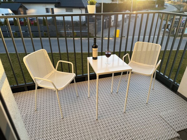 A balcony with two white mesh chairs, a small table, a bottle of wine, and a glass. - Stylish seaside escape in Nowe Pogórze! Relax & enjoy the view! Wifi free (Pogórze)