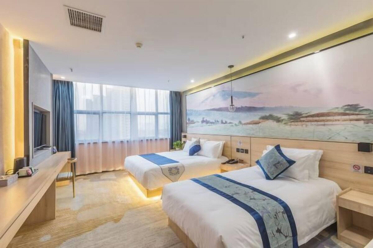 A hotel room with two beds, a desk, a TV, and a large window.