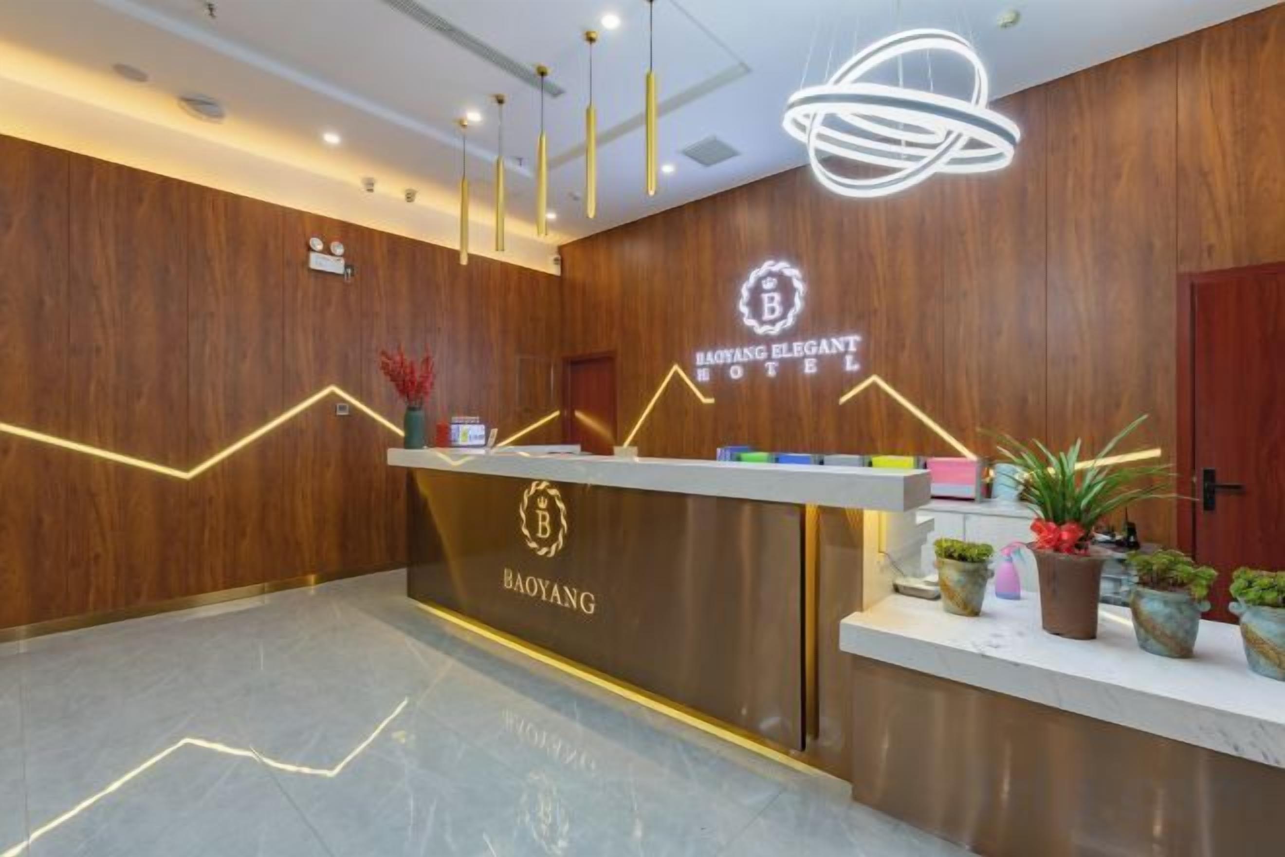 Un mostrador de recepción con terminación de madera y un logotipo, un área de recepción con piso de mármol y un techo con luces colgantes.