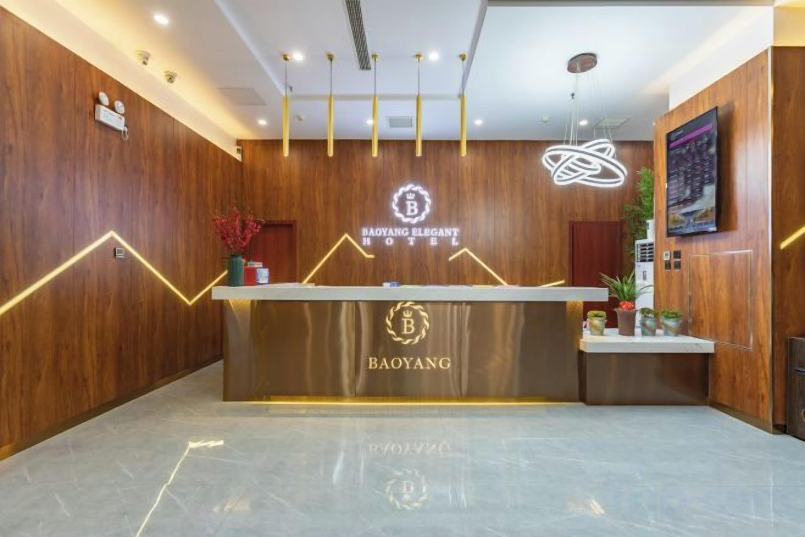 Taulell de recepció d'hotel amb acabat de fusta, un logotip i una làmpada moderna.