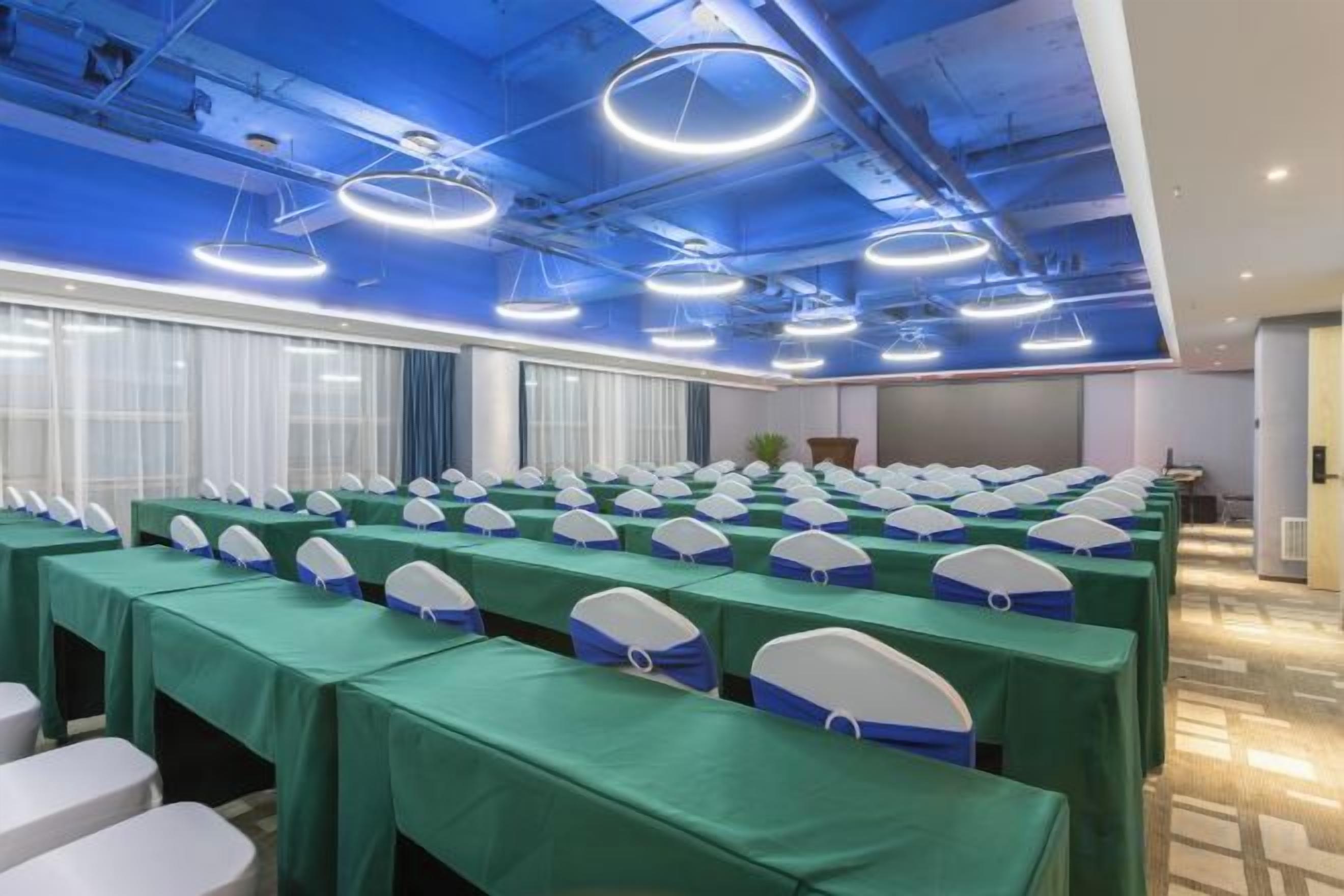 Une salle de conférence avec des rangées de tables, chacune recouverte d’une nappe verte et entourée de chaises blanches.