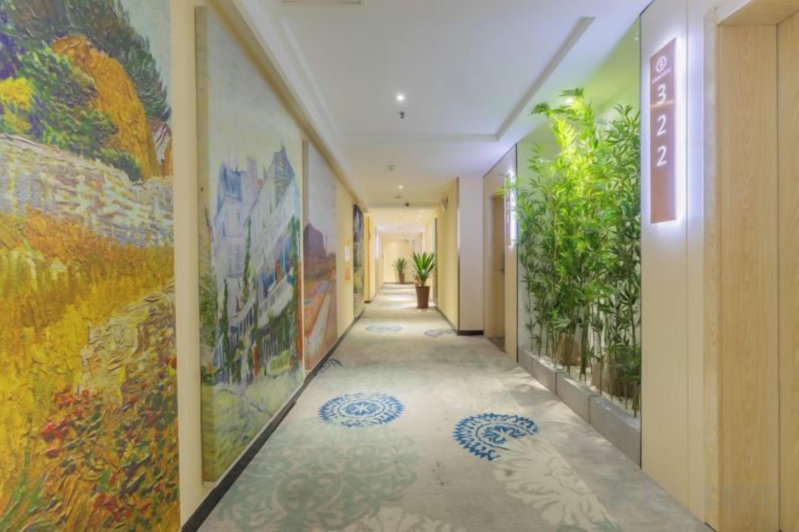 Un pasillo de hotel con una larga galería, pinturas grandes en las paredes y una planta en maceta a la derecha.