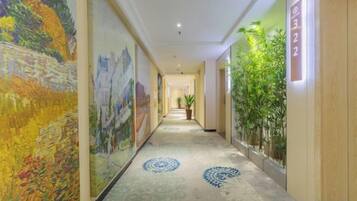 Un pasillo de hotel con una larga galería, pinturas grandes en las paredes y una planta en maceta a la derecha.