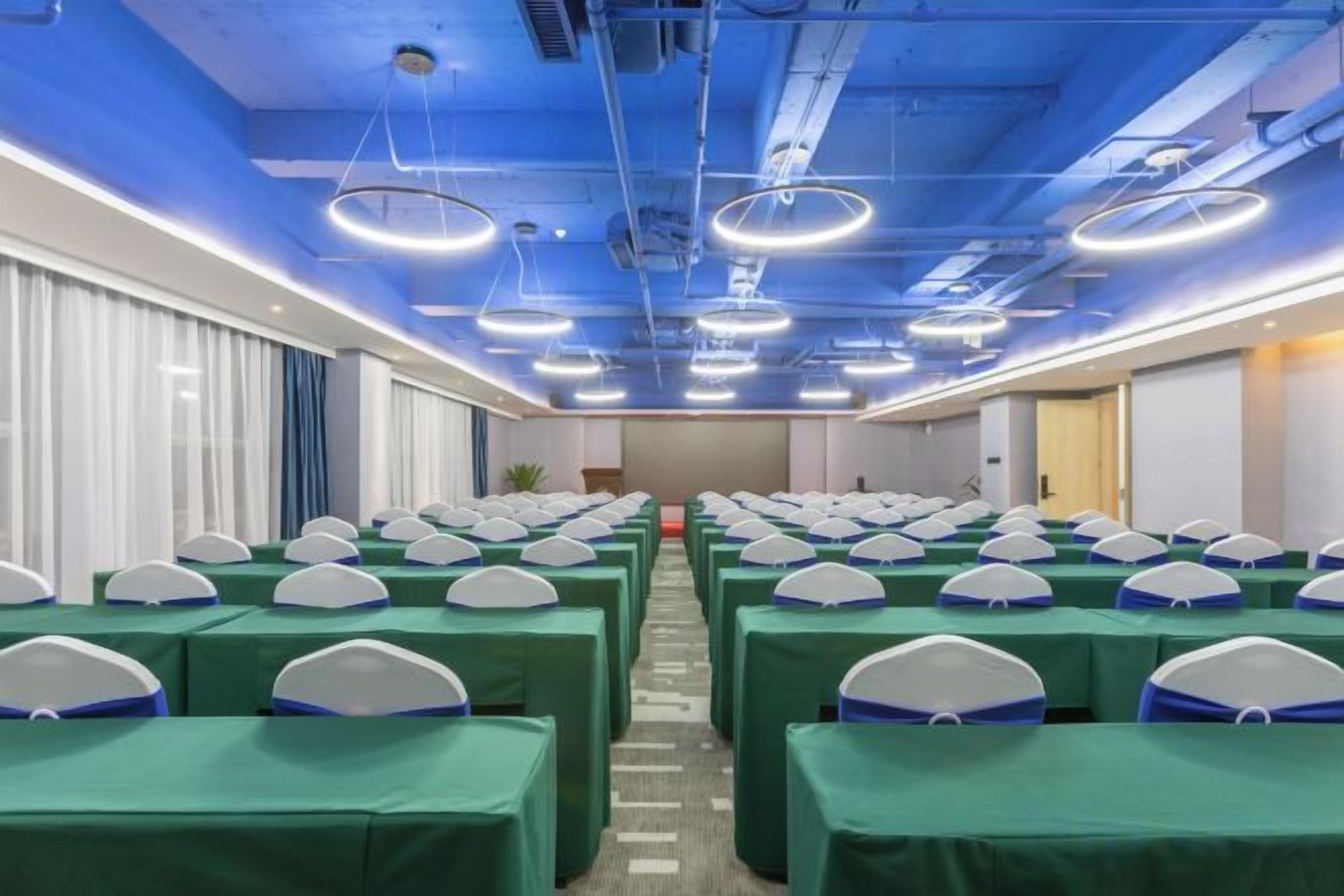 Un salón de conferencias con filas de mesas y sillas, techo azul e iluminación moderna.