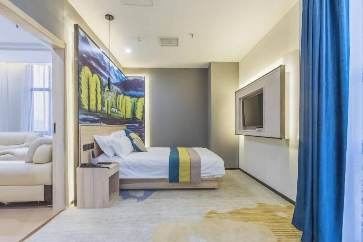 A modern hotel room with a bed, a sofa, a TV, and a painting on the wall.