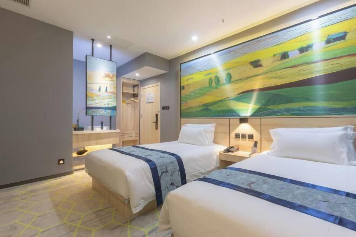 A hotel room with two beds, a large painting on the wall, a desk, and a wardrobe.