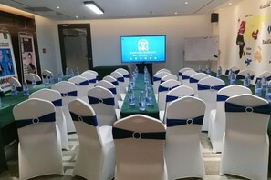 A conference room with rows of white chairs with blue sashes, a long table with water bottles, and a screen displaying text. - Baoyang Boutique Hotel (Shijiazhuang North Zhonghua Street Zhongchu Plaza) (Shijiazhuang)