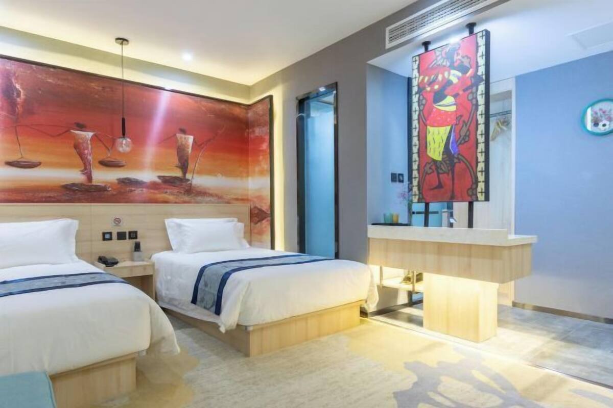 A hotel room with two beds, a large abstract painting on the wall, a bathroom with a mirror, and a small round table.