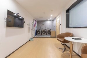 A laundry room with a washing machine, dryer, and a small table with chairs. - Baoyang Boutique Hotel (Shijiazhuang North Zhonghua Street Zhongchu Plaza) (Shijiazhuang)