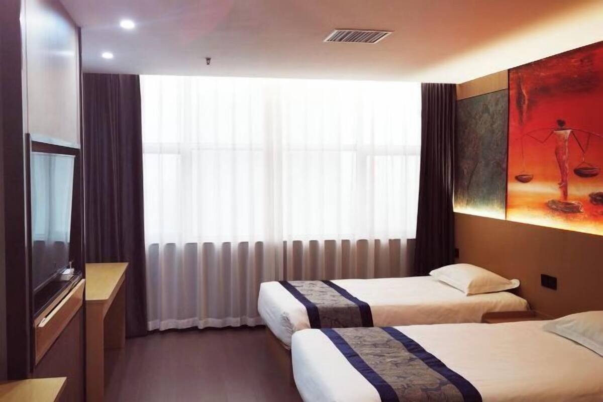 A hotel room with two beds, a TV, a large window with curtains, and a painting on the wall.