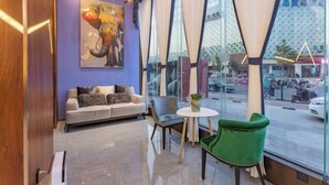 A modern hotel lobby with a sofa, chairs, a small table, and a large window offering a view of the street. - Baoyang Boutique Hotel (Shijiazhuang North Zhonghua Street Zhongchu Plaza) (Shijiazhuang)