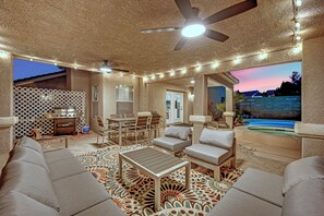 An outdoor patio with a ceiling fan, string lights, a grill, and a pool.