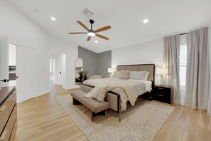 A spacious bedroom with a large bed, a ceiling fan, a bedside table with a lamp, and a bench at the foot of the bed.