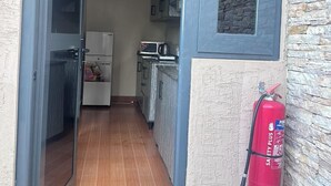 Un couloir étroit mène à une cuisine équipée d’un réfrigérateur, d’un four à micro-ondes et de placards. Un extincteur est fixé au mur.