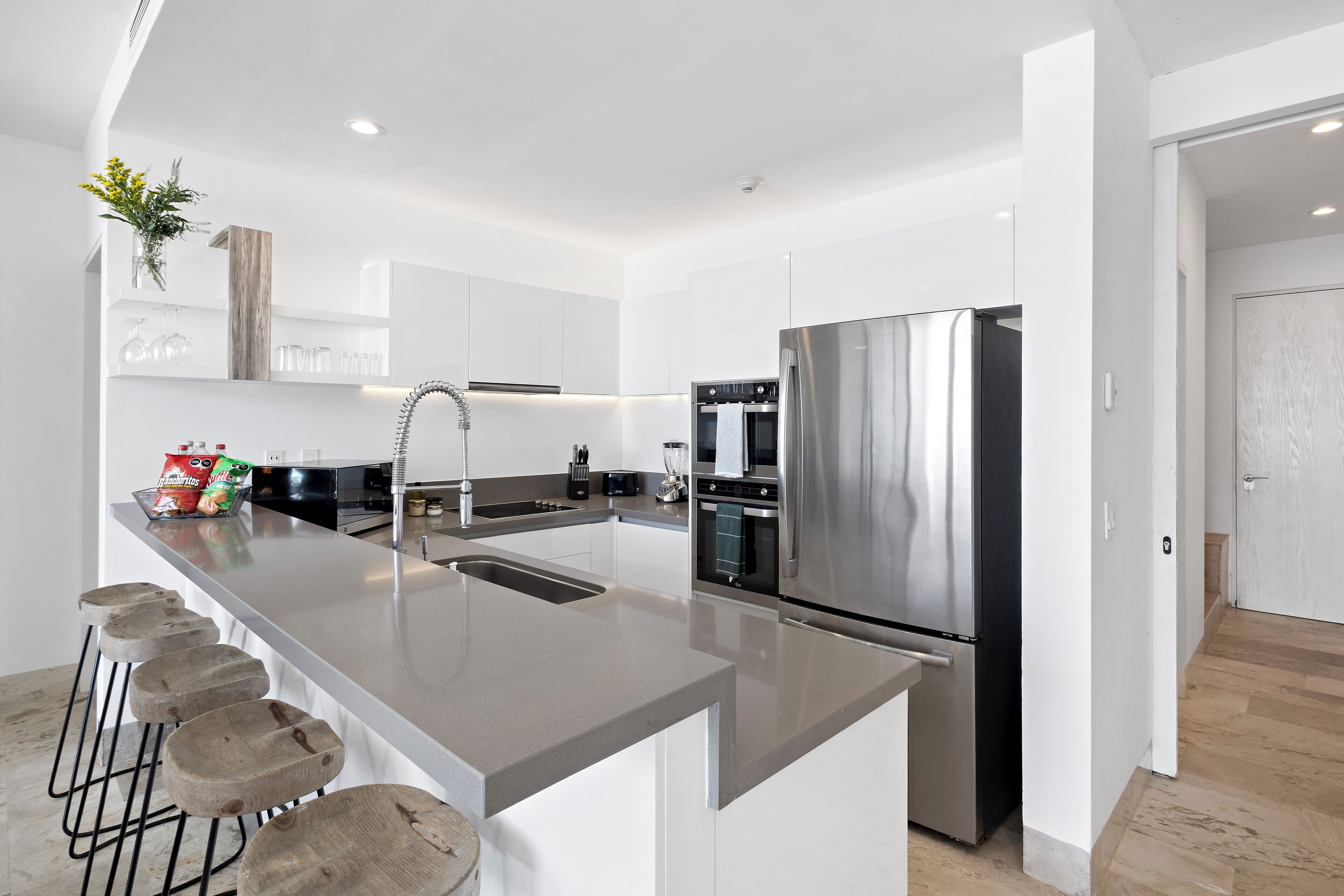 A modern kitchen with a stainless steel refrigerator, a built-in oven, and a large island with stools.