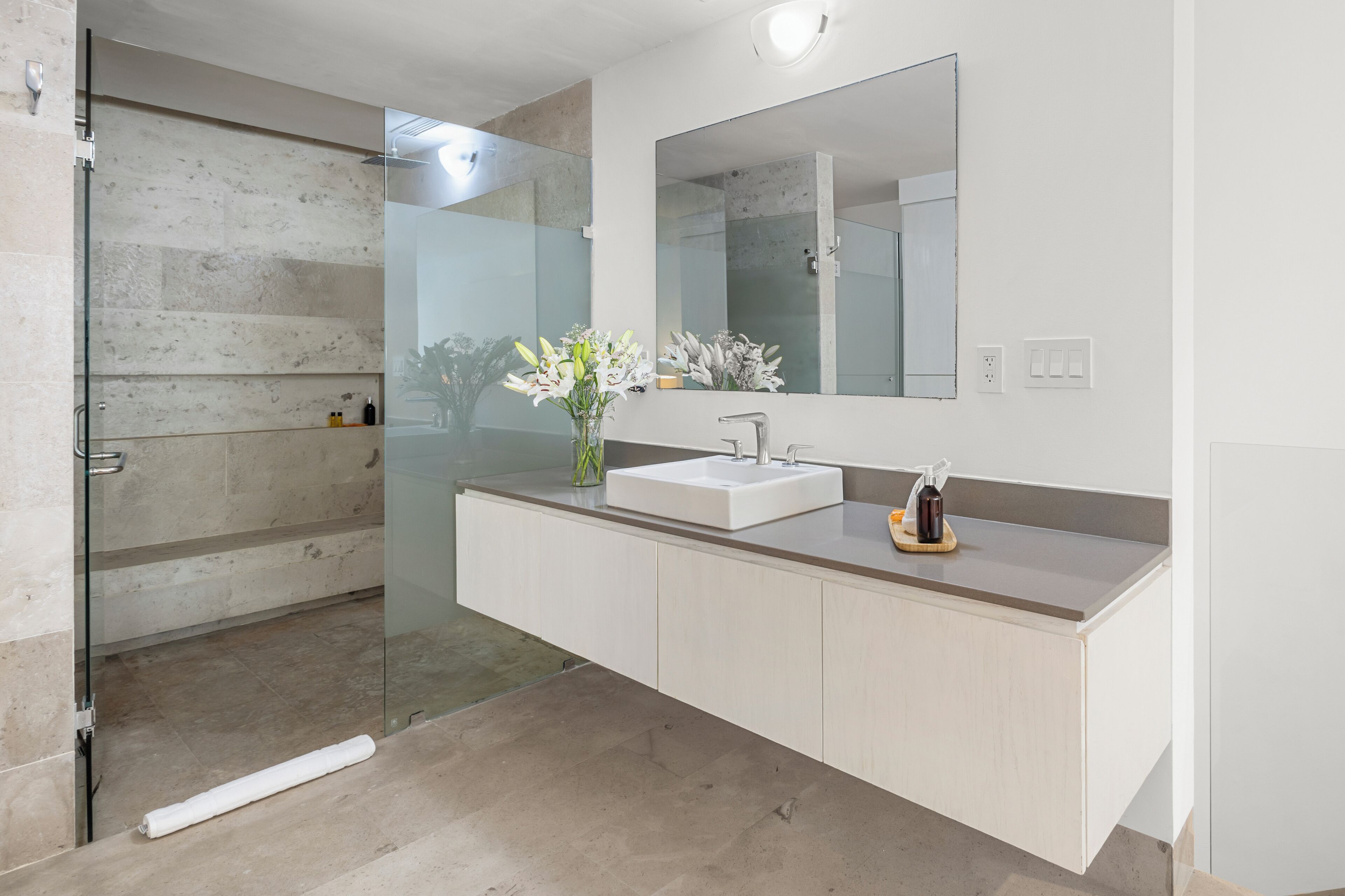 A modern bathroom with a glass shower enclosure, a white sink, and a large mirror.