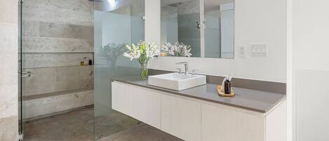Un baño moderno con cabina de ducha de vidrio, un lavabo blanco y un espejo grande.