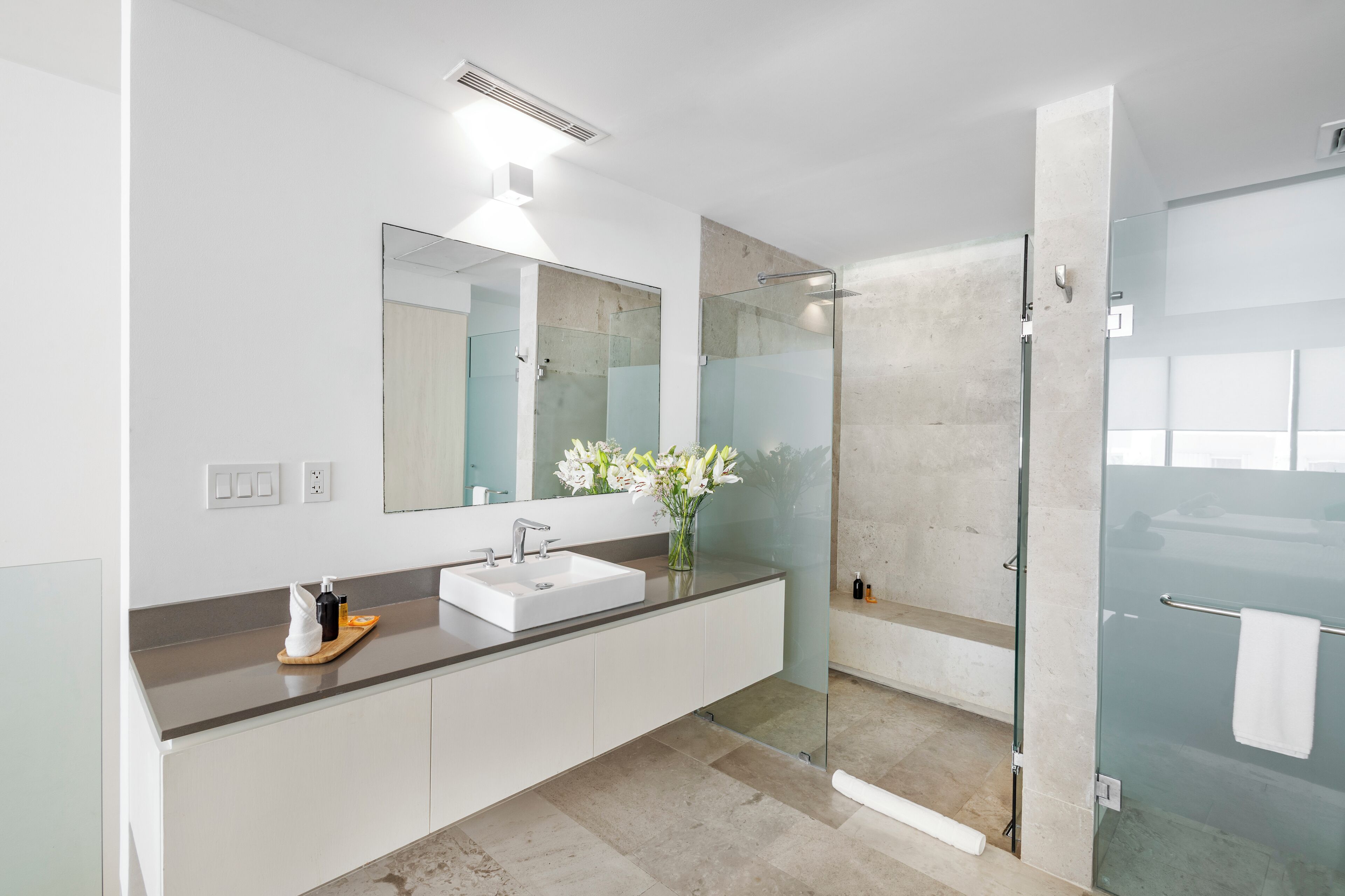 A modern bathroom with a white sink, a large mirror, and a glass shower enclosure.