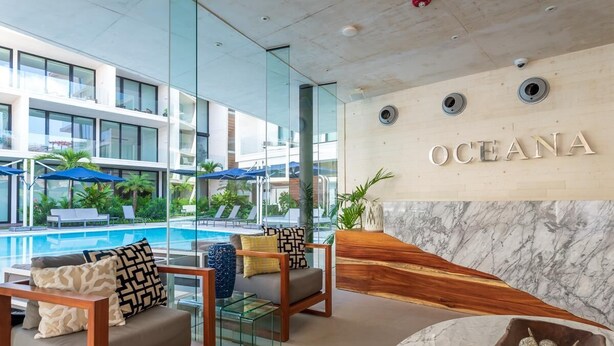 Un hall d’hôtel moderne doté d’un espace piscine, de sièges confortables et d’un comptoir d’accueil en marbre.