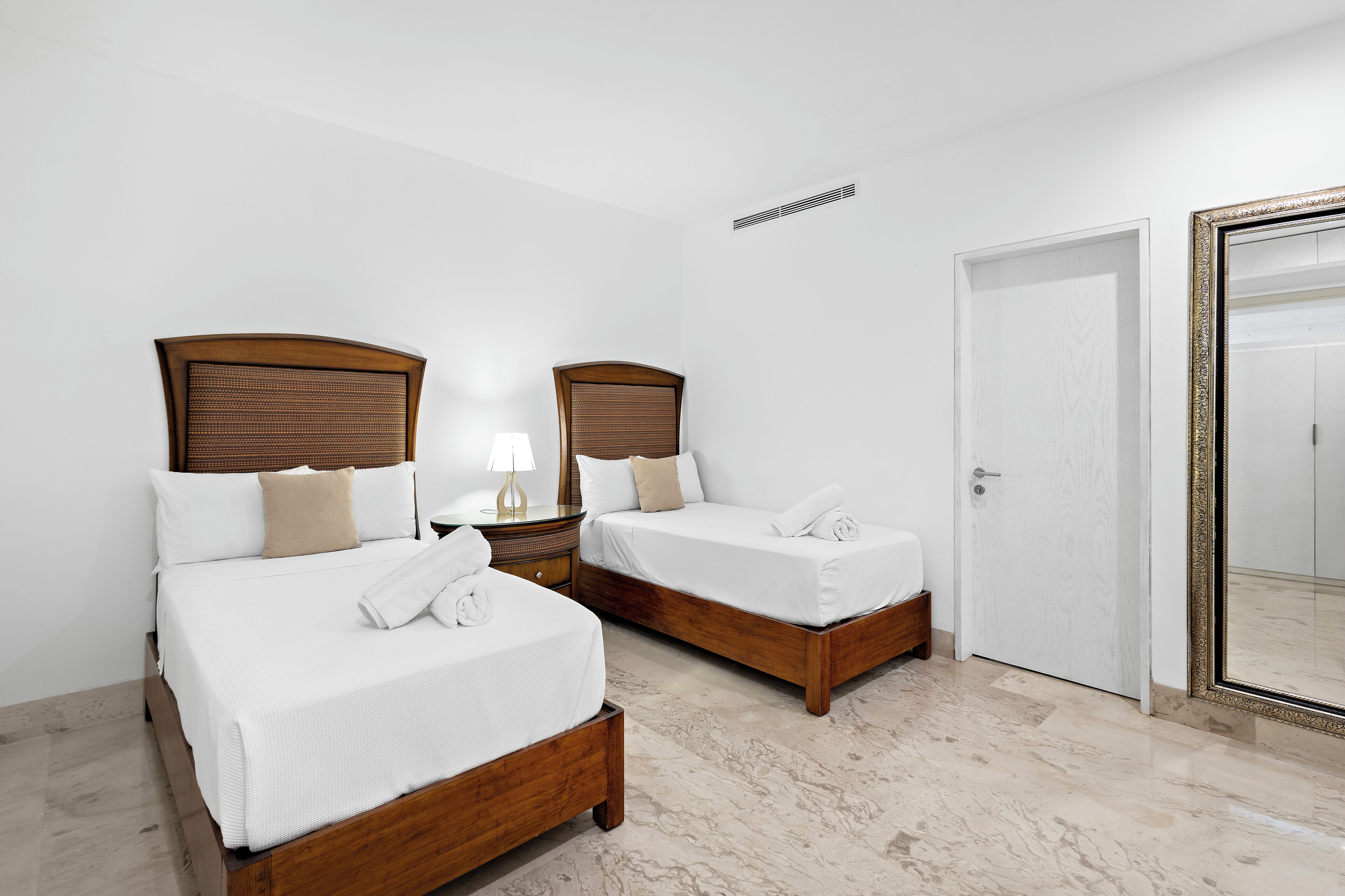 Een hotelkamer met twee houten bedden, wit beddengoed, een nachtkastje met een lamp en een grote spiegel aan de muur.