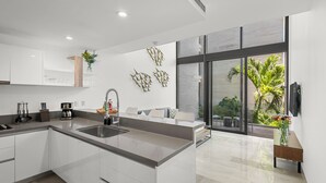 Une cuisine moderne dotée d’un grand îlot central, de meubles blancs et offrant une vue sur la verdure environnante.