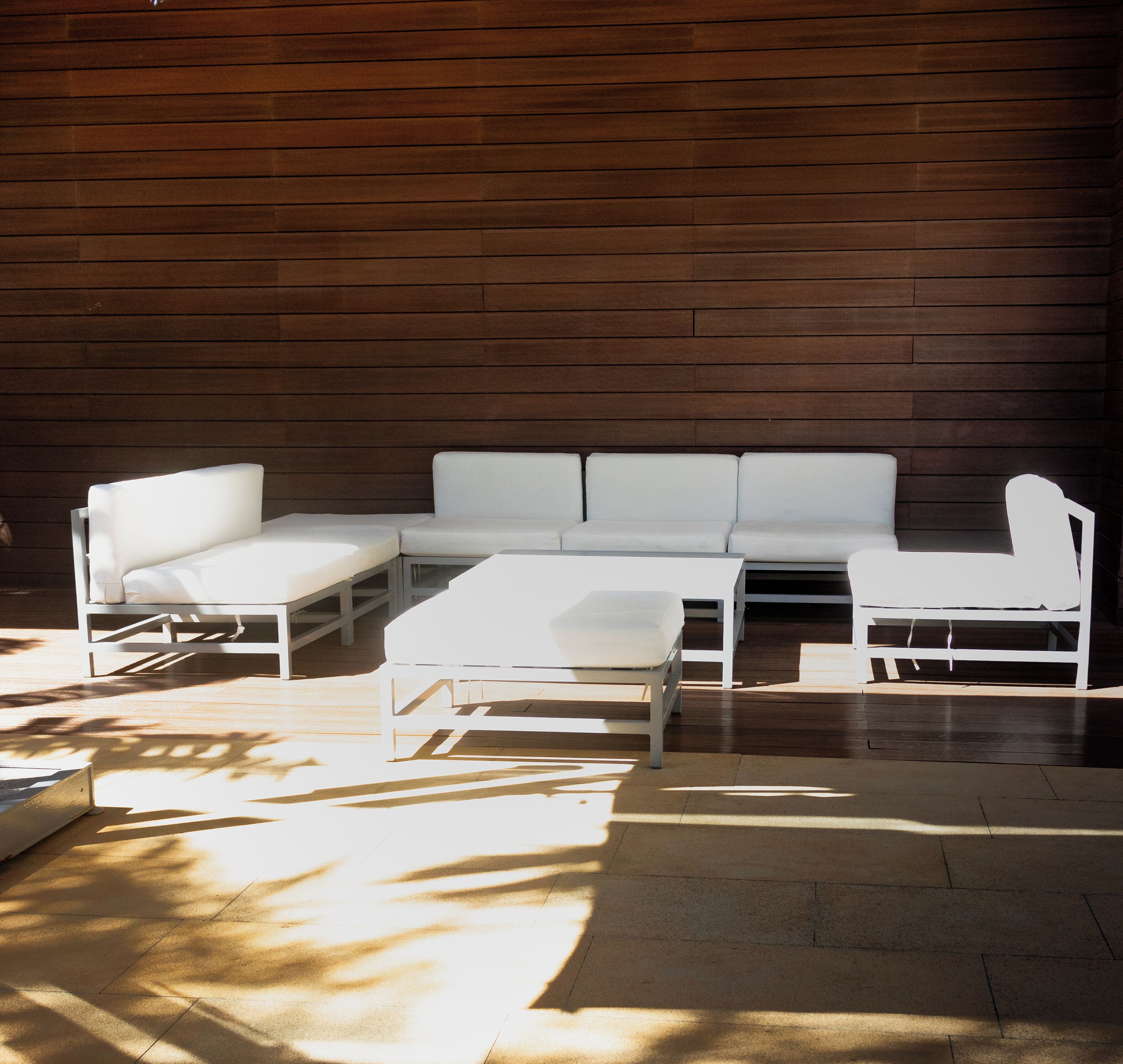 A modern outdoor seating area with a sectional sofa and a small table, set against a wooden wall.