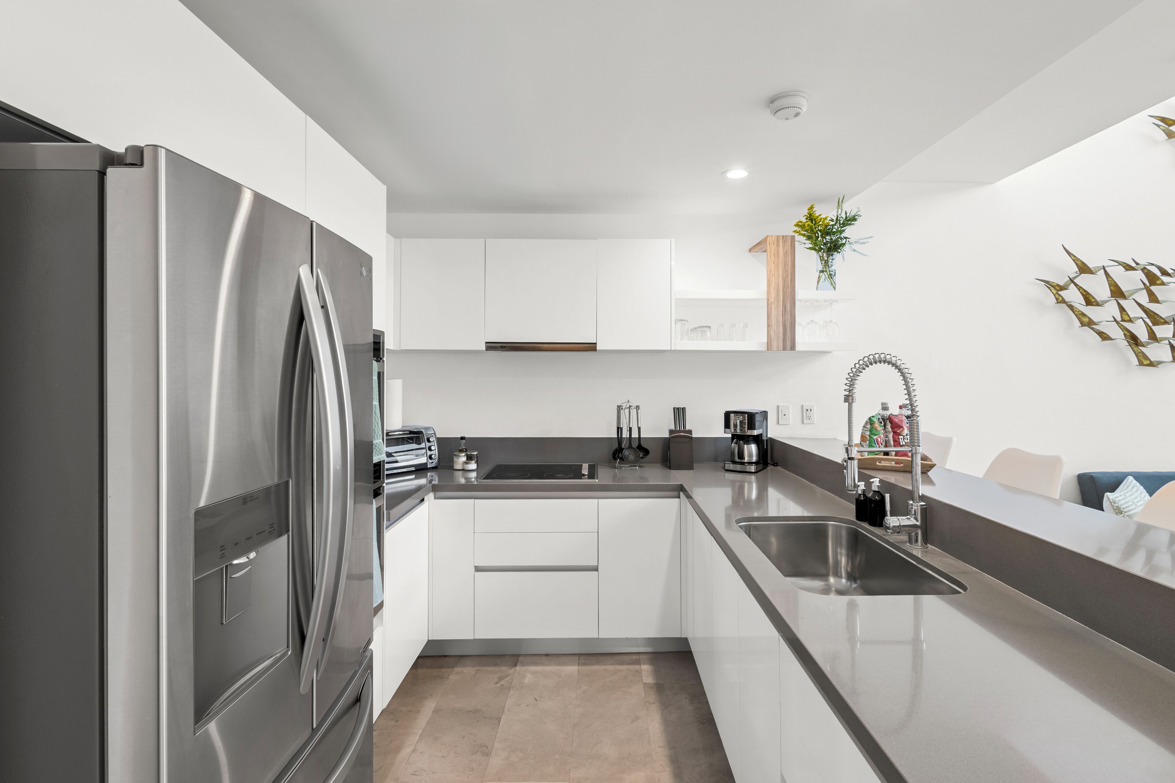 A modern kitchen with a stainless steel refrigerator, white cabinets, a double sink, and a coffee maker.