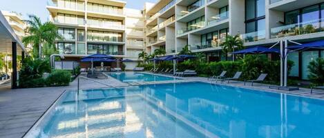 Un hotel moderno con piscina central, varios balcones y zonas de estar al aire libre.