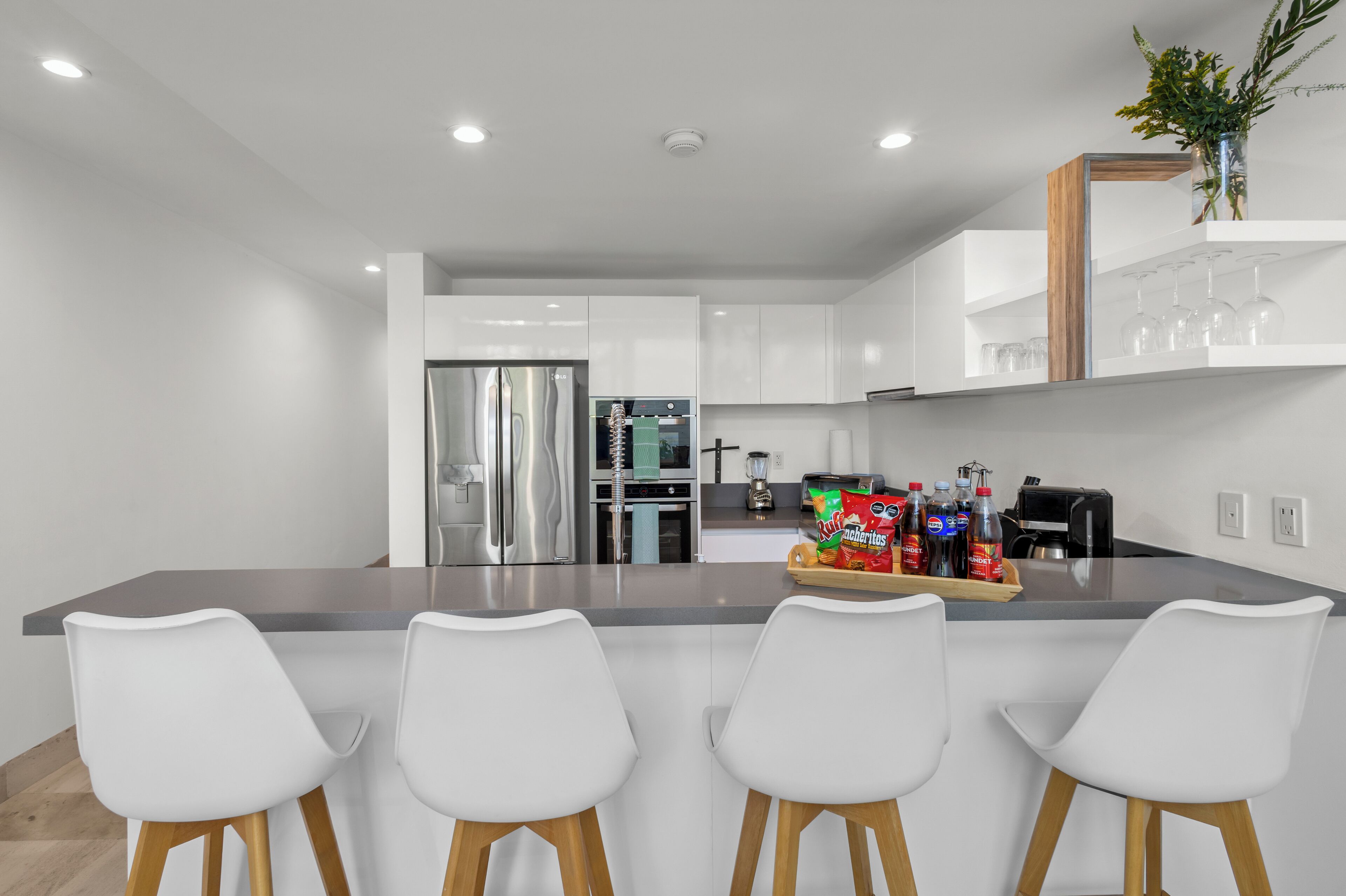 A modern kitchen with white cabinetry, a central island with bar stools, stainless steel appliances, and a coffee machine.