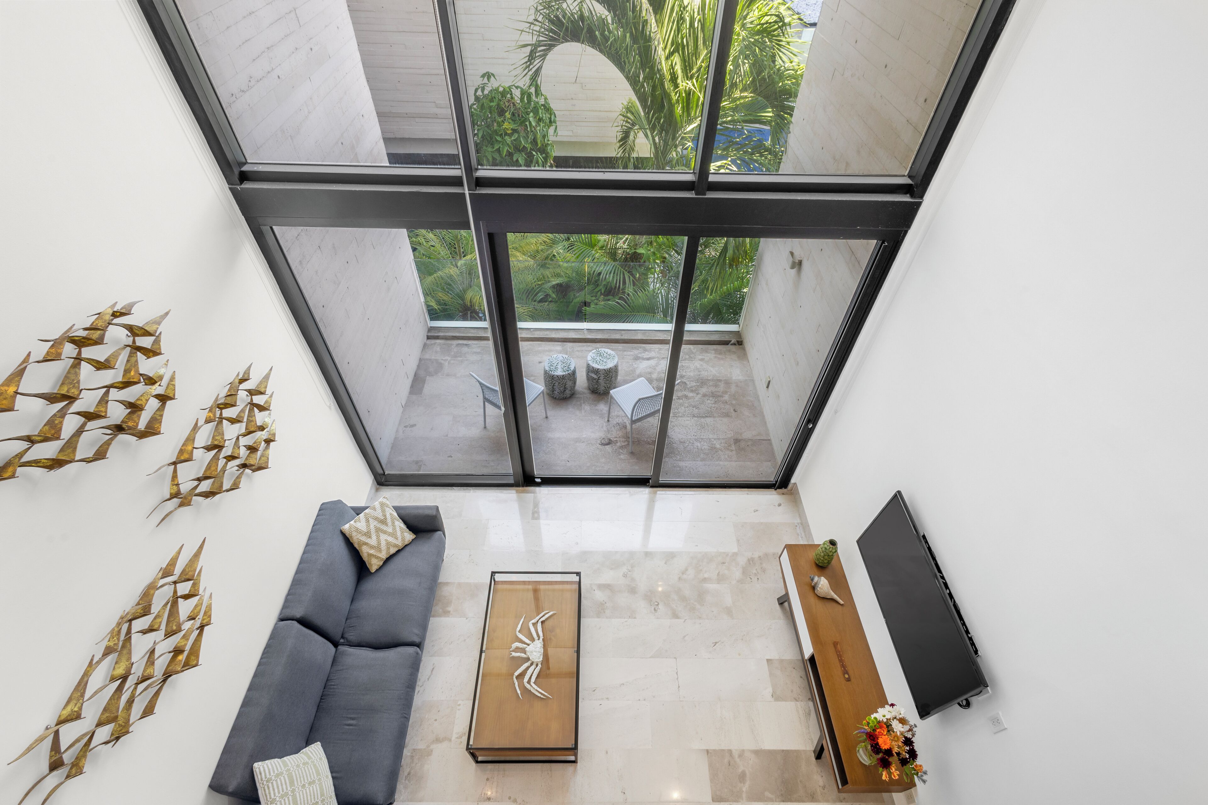 A modern living room with a large glass window, a grey sofa, a wooden coffee table, and a flat-screen TV.