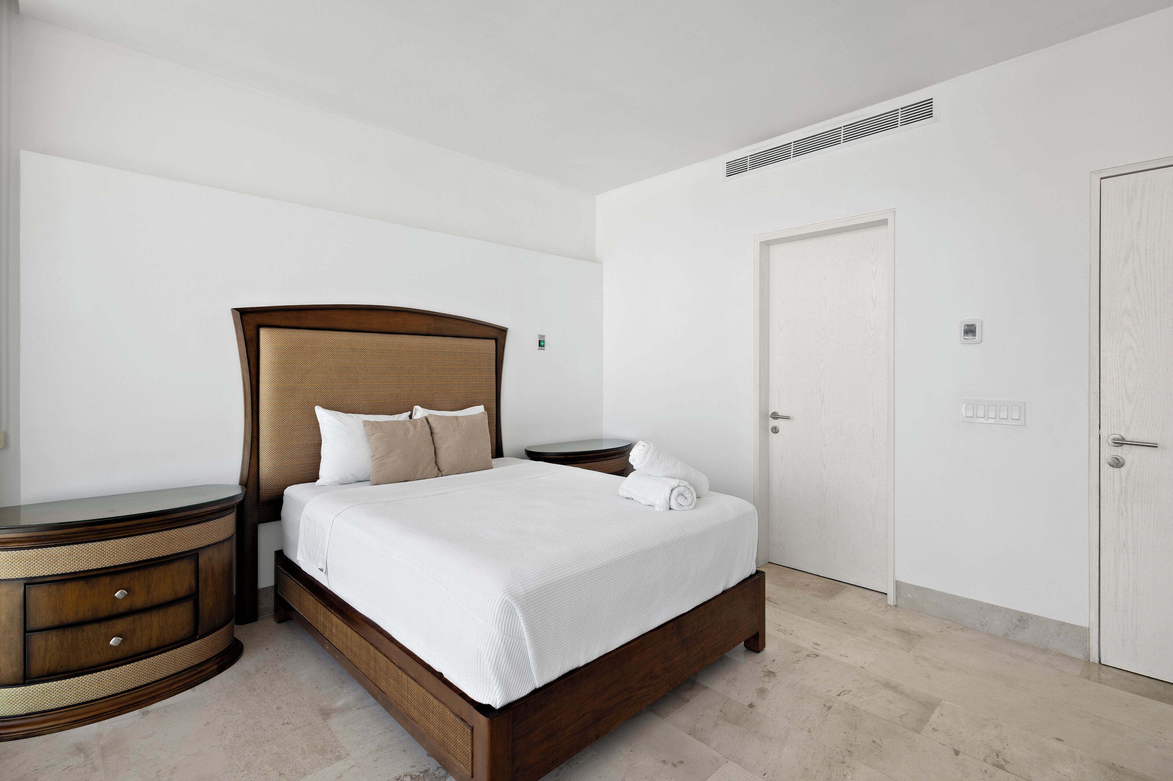 A neatly arranged bedroom with a large bed, a bedside table, a nightstand, and a wardrobe.