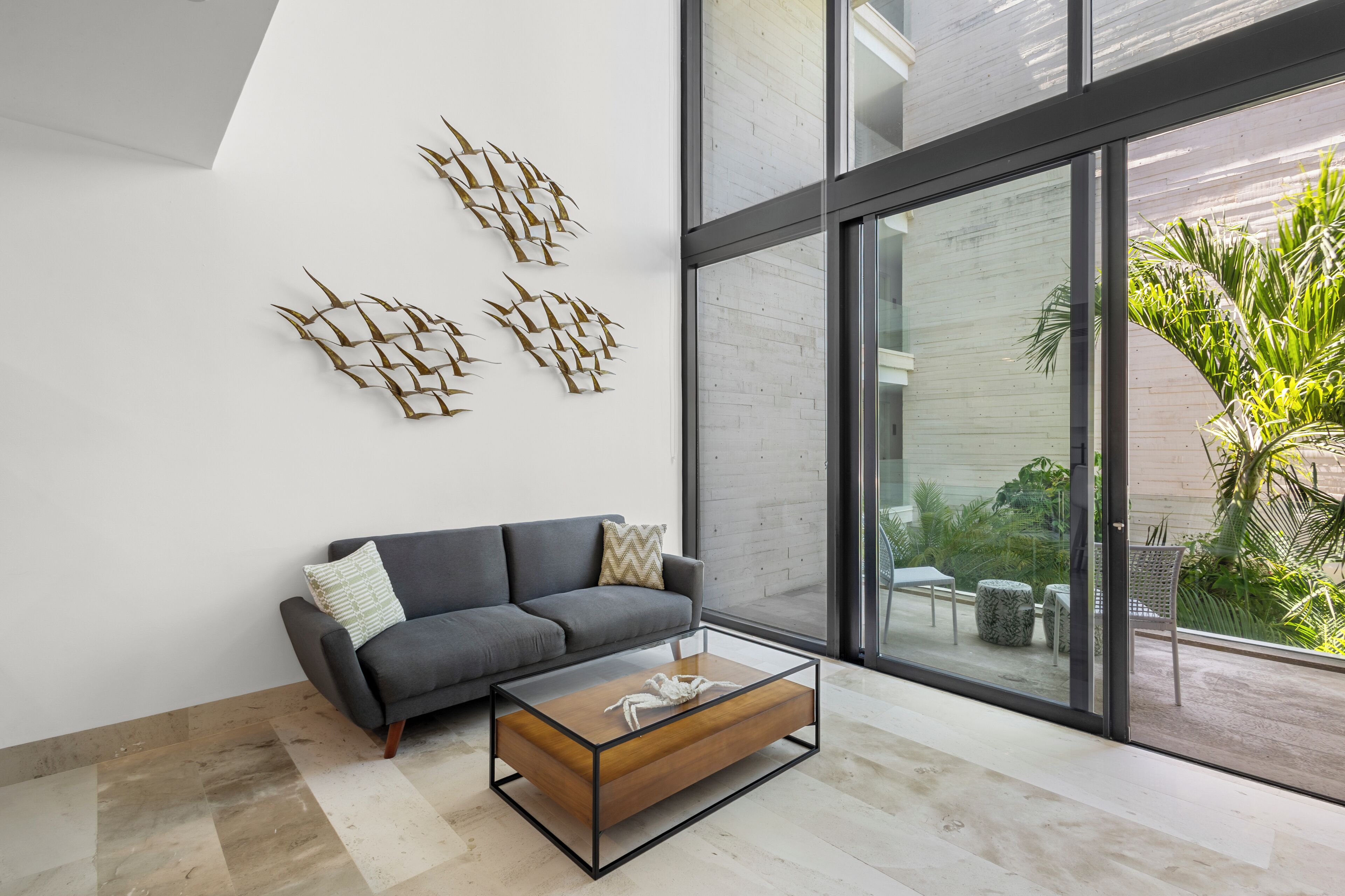Ein modernes Wohnzimmer mit grauem Sofa, einem Glastisch und abstrakten Wandbildern.