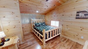A wooden cabin room with a bed, a window, and a lamp on a side table.