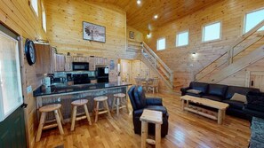 A spacious cabin interior with a wooden interior, a kitchen area, a dining area, and a staircase.