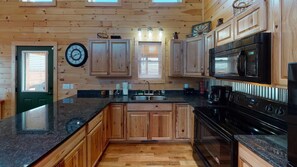 A wooden-paneled kitchen with a granite countertop, a black stove, and a microwave.