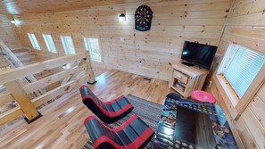 A wooden cabin interior with a loft area, a television, and a small table with a red circular object.