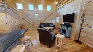 L’intérieur d’une cabane avec un plancher en bois, une cheminée, un canapé, un téléviseur et un escalier.