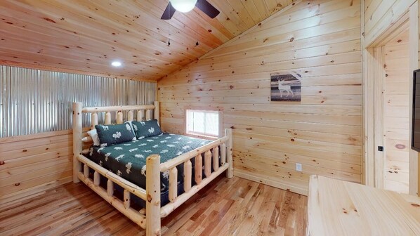 Une pièce de style cabane en bois, avec un lit, une fenêtre et un ventilateur de plafond.