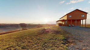 A wooden cabin with a porch, a gravel driveway, and a grassy field.