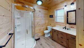 A wooden cabin bathroom with a glass-enclosed shower, a toilet, and wooden cabinets.
