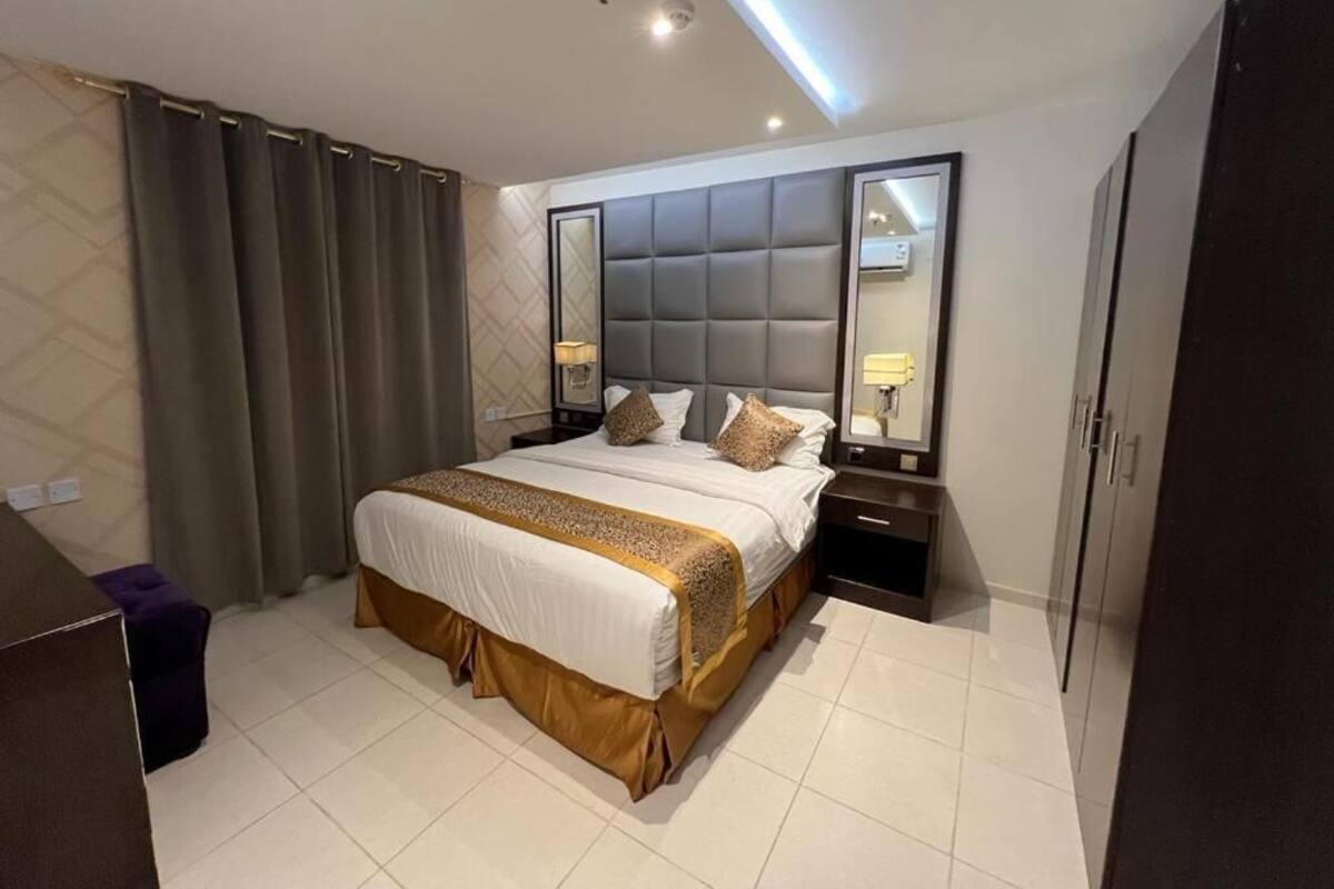 Una habitación de hotel moderna con una cama grande, una mesita de noche, un armario y un espejo.