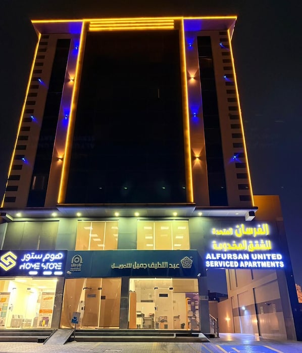 Un edificio con una entrada destacada y señalización de 'ALFURSAN UNITED SERVICE APARTMENTS'.