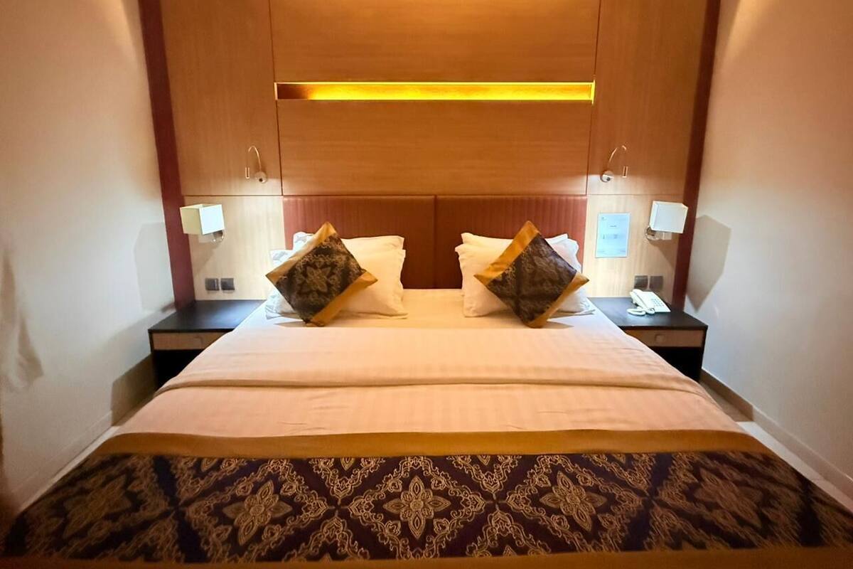 Habitación de hotel con una cama grande, dos mesitas de noche y cabecera con iluminaci ón integrada.